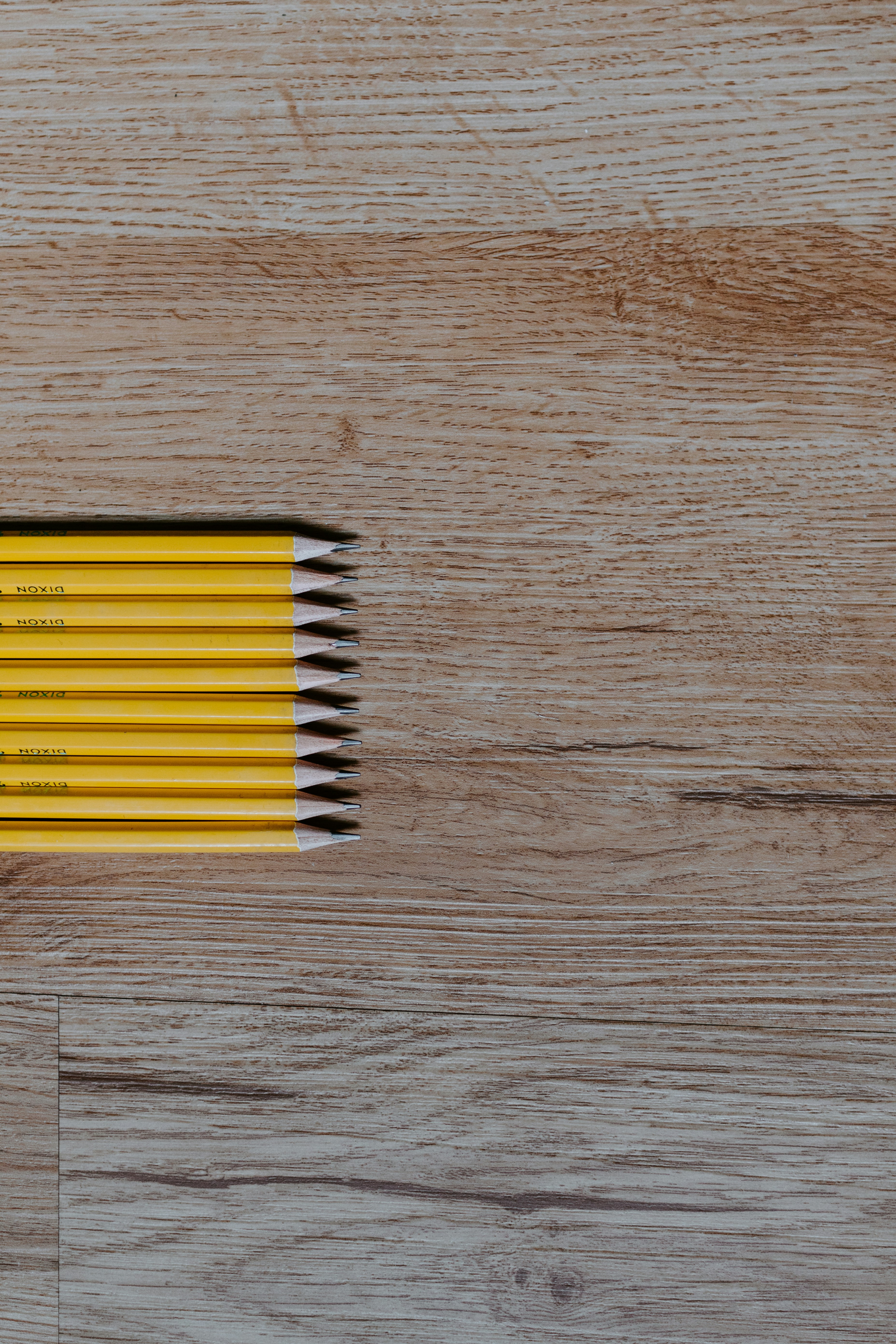 Photograph of a wood desktop with 10 yellow pencils lying horizontally on the left side